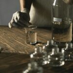 O nas Crop anonymous female in latex gloves making fluid for perfume among glass jars on wooden table